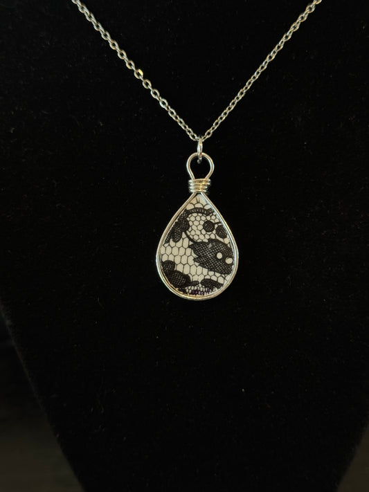 Teardrop-shaped pendant with black and white pattern on a chain against a black background