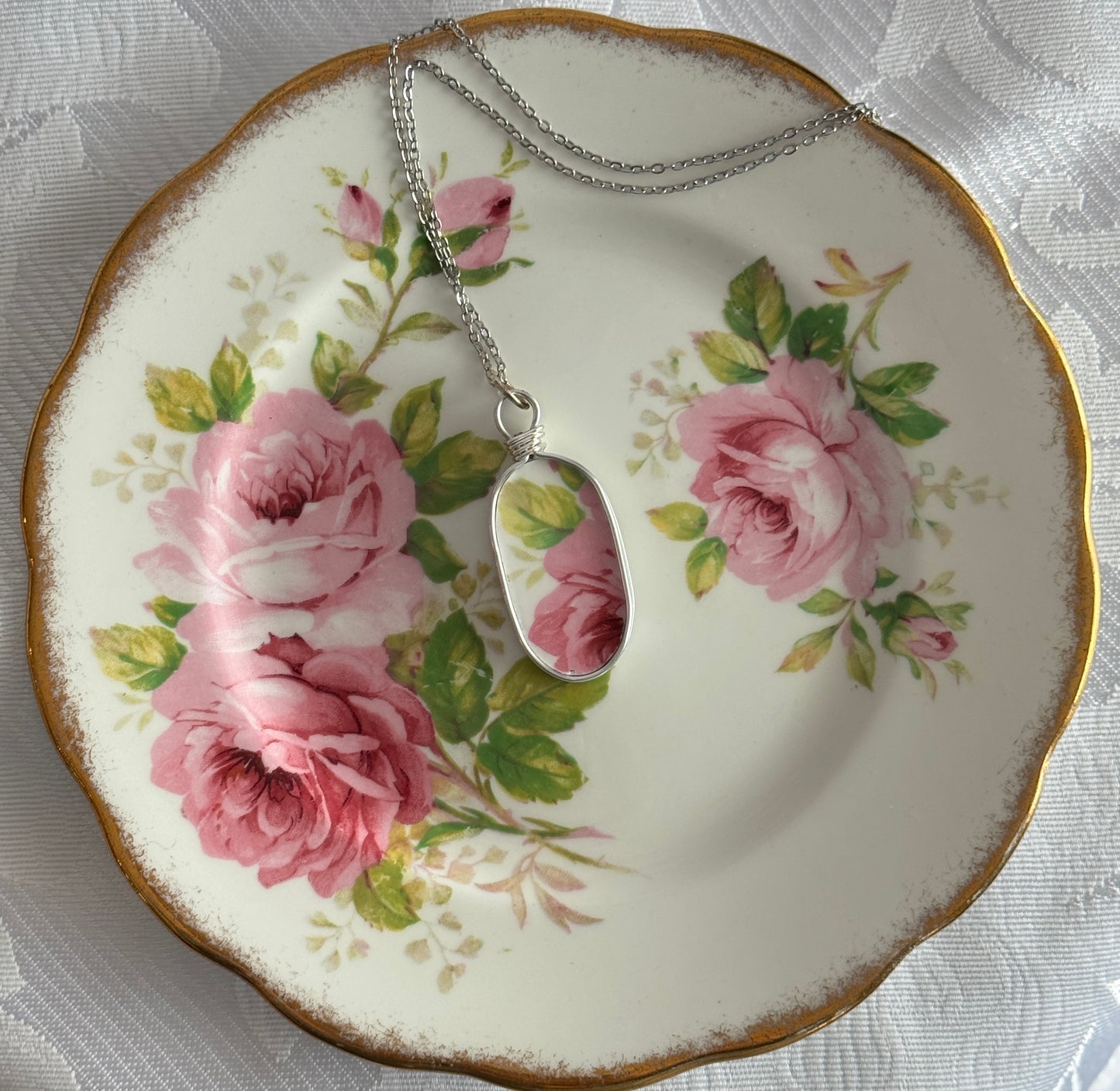 Necklace with a pendant on a decorative plate featuring pink roses.