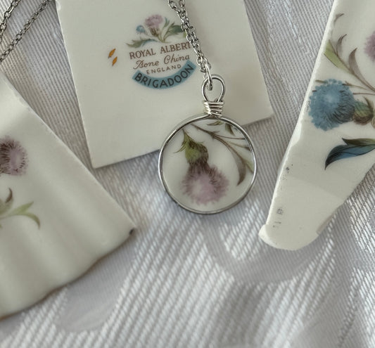 Necklace with a round pendant featuring pressed flowers on a floral-patterned card with 'Royal Albert' branding.