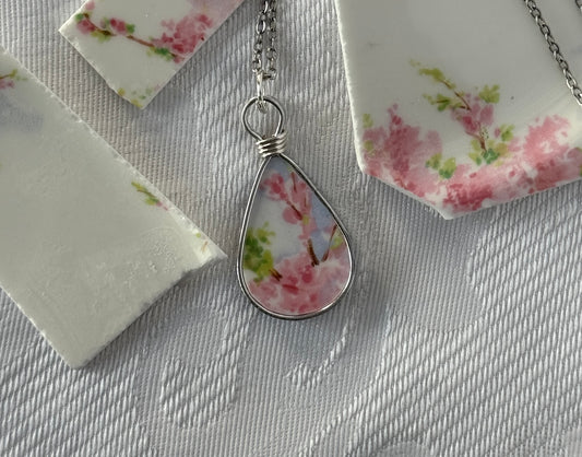 Teardrop-shaped floral pendant on a chain against a floral-patterned background