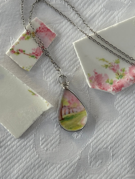 Teardrop-shaped pendant with floral design on a chain, displayed on a textured surface.