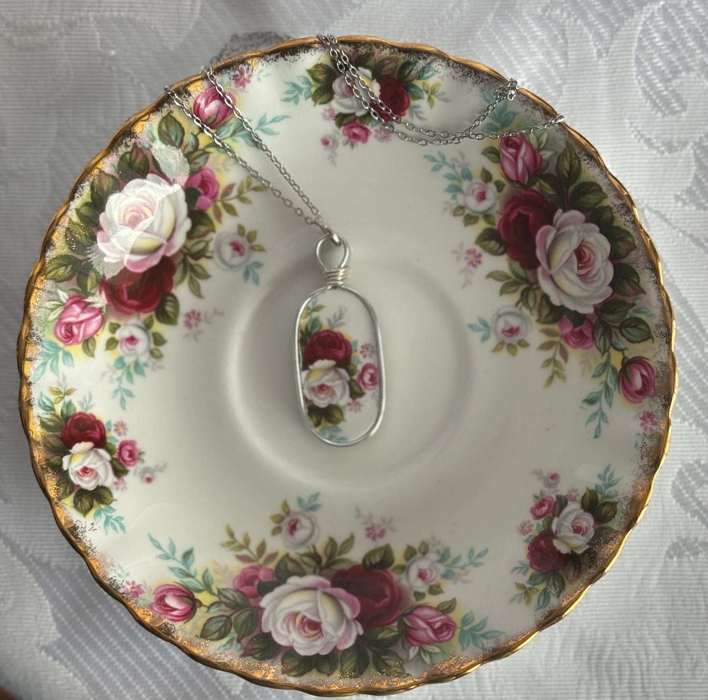 Floral teacup with a pendant featuring a similar floral design on a textured surface.