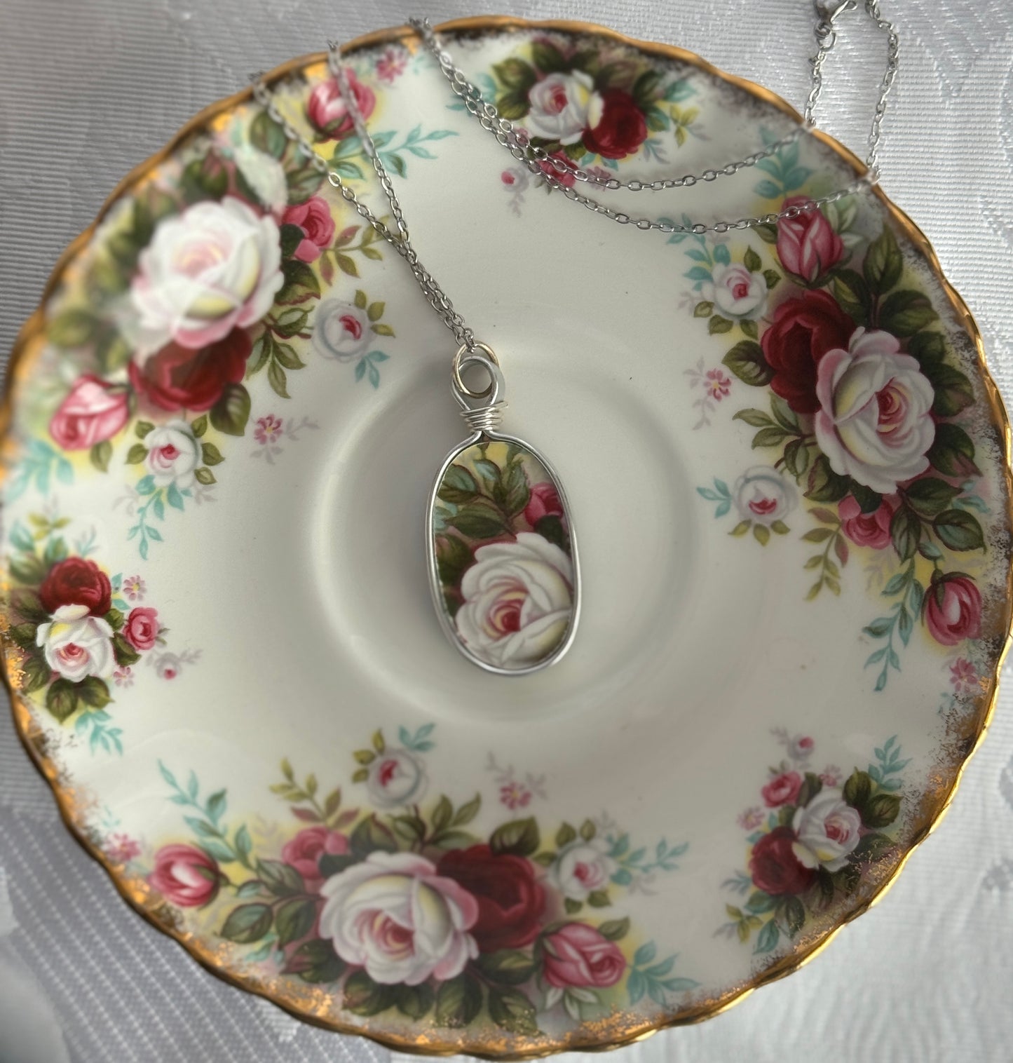 Tea cup with floral design and a necklace with a rose pendant on a matching saucer.