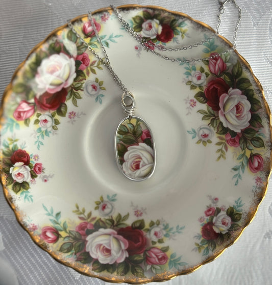 Tea cup with floral design and a necklace with a rose pendant on a matching saucer.