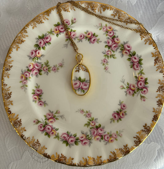 Decorative plate with floral pattern and a gold necklace with a pendant on a white lace background
