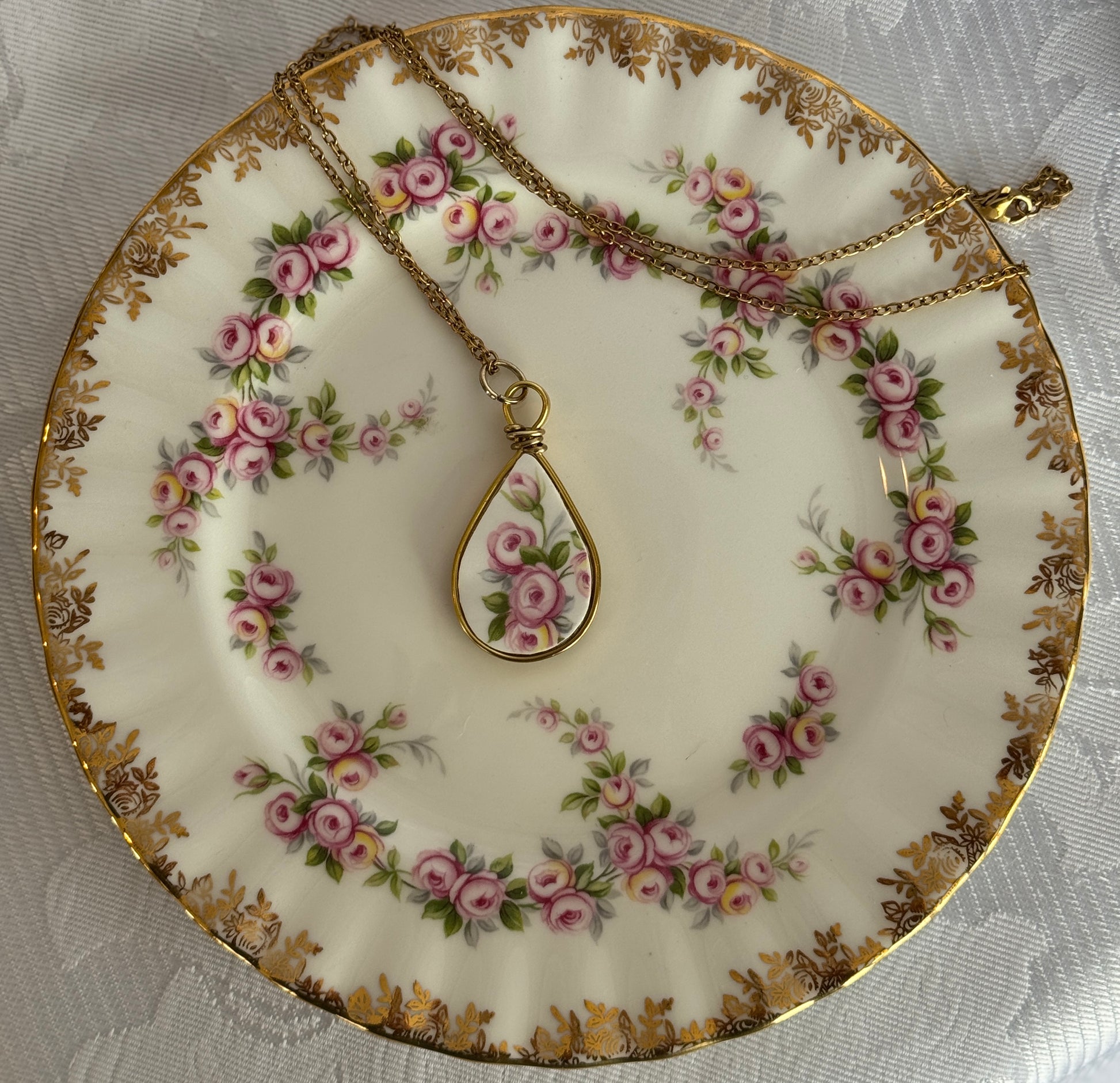 Tea plate with floral design and a gold necklace with a teardrop pendant on a white lace background