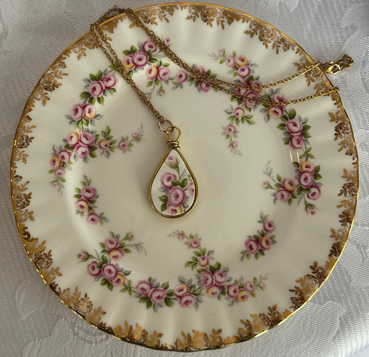 Tea plate with floral design and a gold necklace with a teardrop pendant on a white lace background