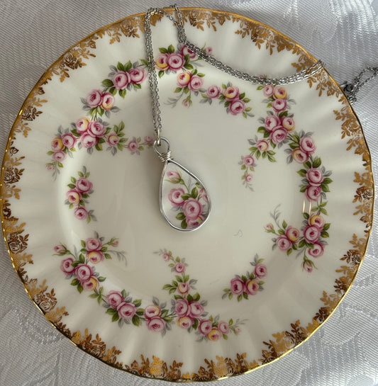 Tea plate with floral design featuring a necklace with a teardrop pendant.
