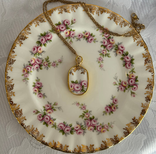 Decorative plate with floral patterns and a gold necklace with a pendant on a textured surface.