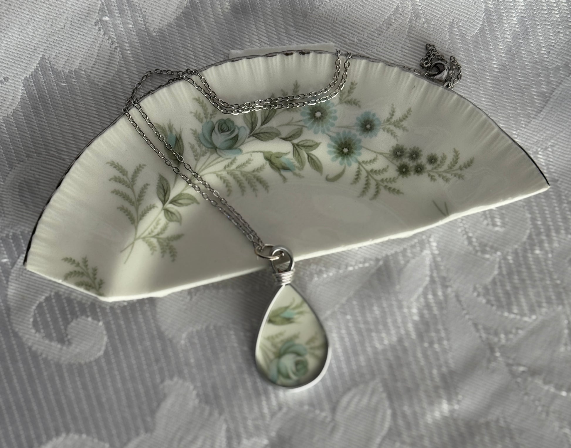 Teardrop-shaped pendant with floral design on a floral-patterned fabric background
