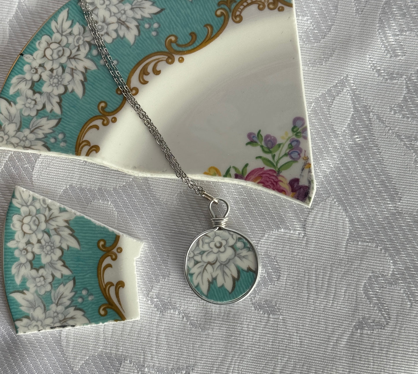 Silver necklace with a floral pendant on a decorative card with floral patterns.