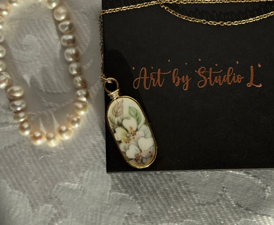 Necklace with a floral pendant on a black card with 'Art by Studio L' text, pearl necklace on gray fabric background