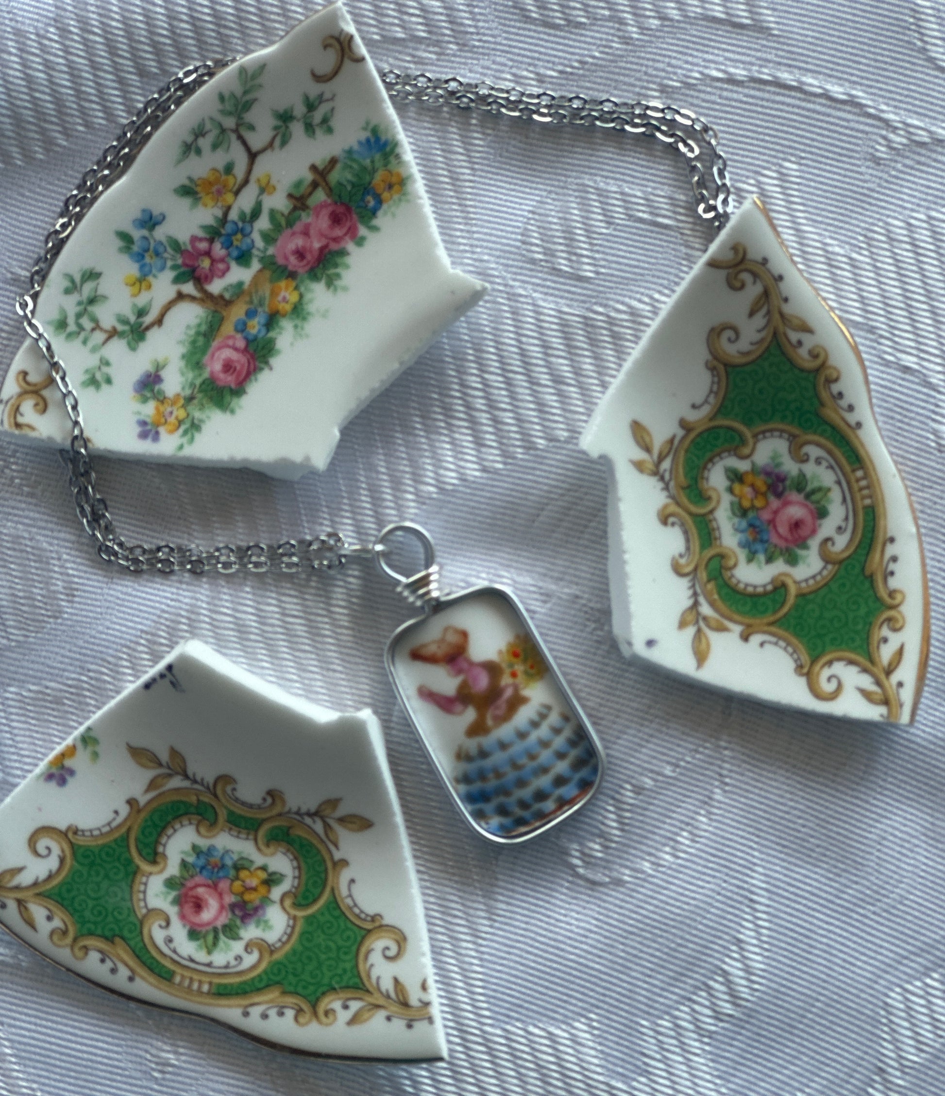 Three decorative ceramic with floral and floral patterns on a chain on a pendant with a lady in a bonnet against a textured background.