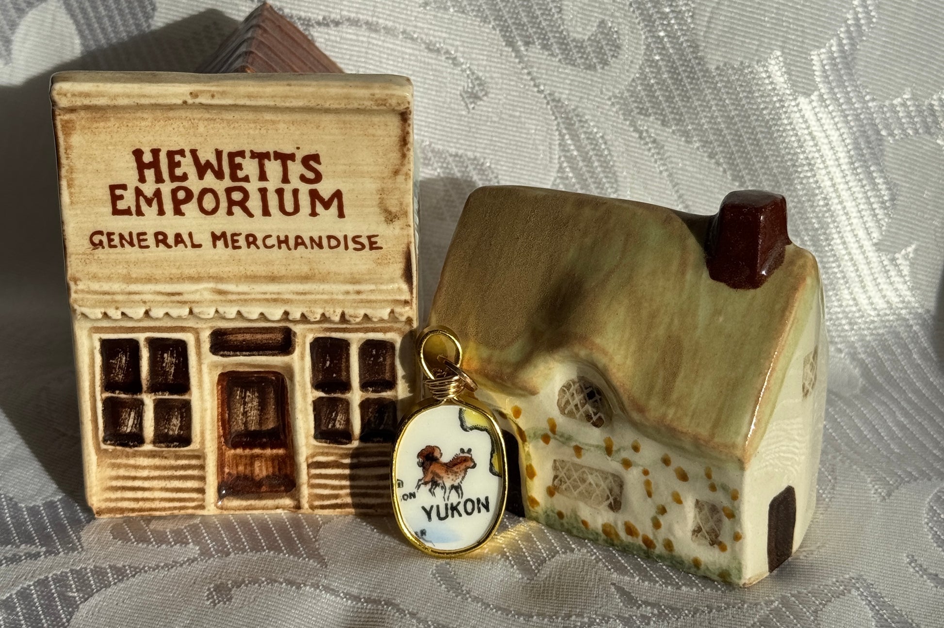 Miniature model of a store front with 'Hewett's Emporium' and a small house, on a textured surface.