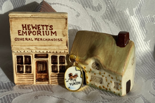 Miniature model of a store front with 'Hewett's Emporium' and a small house, on a textured surface.