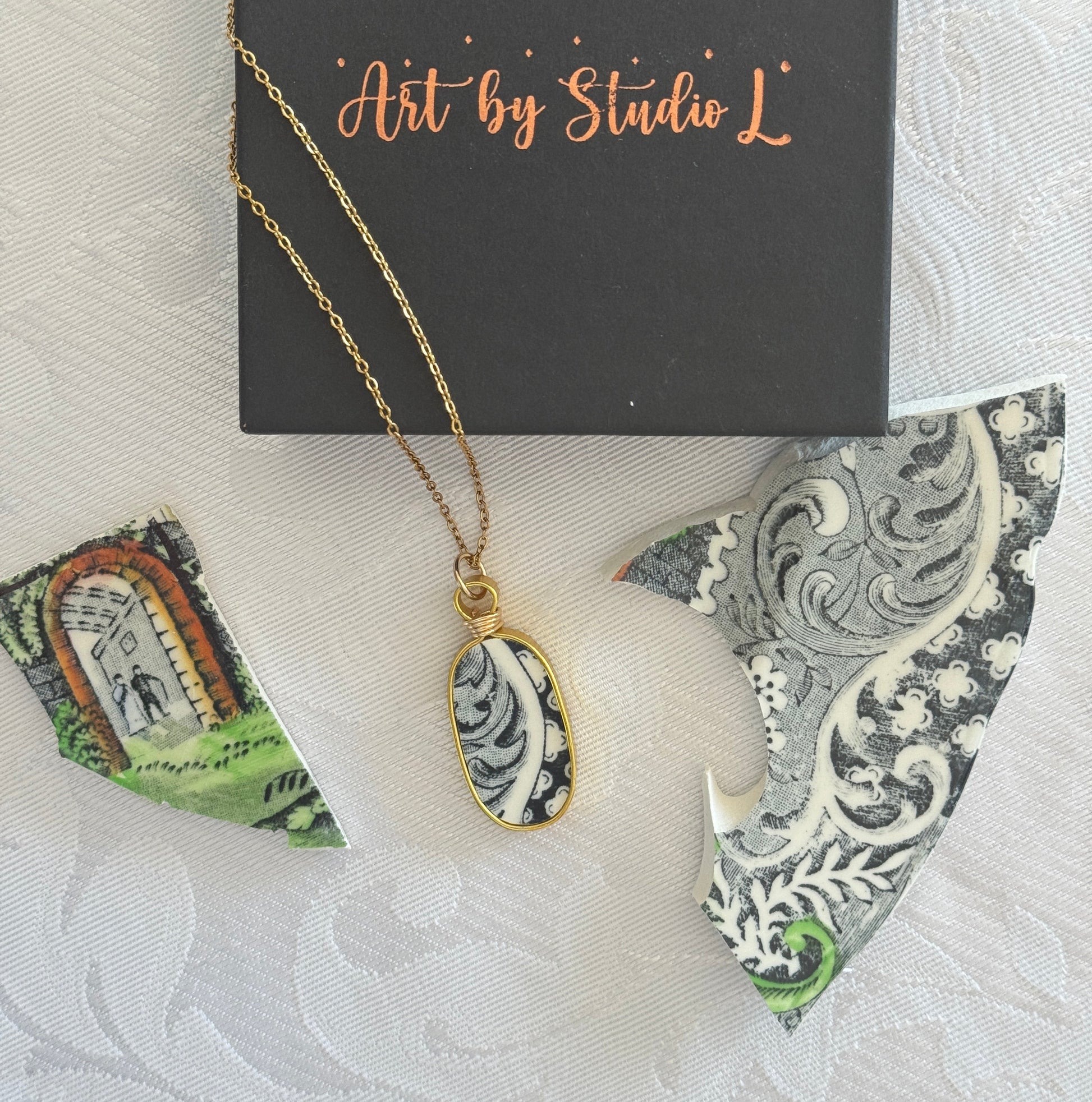 Necklace with a decorative pendant on a card labeled 'Art by Studio L' with a white and gray patterned background.