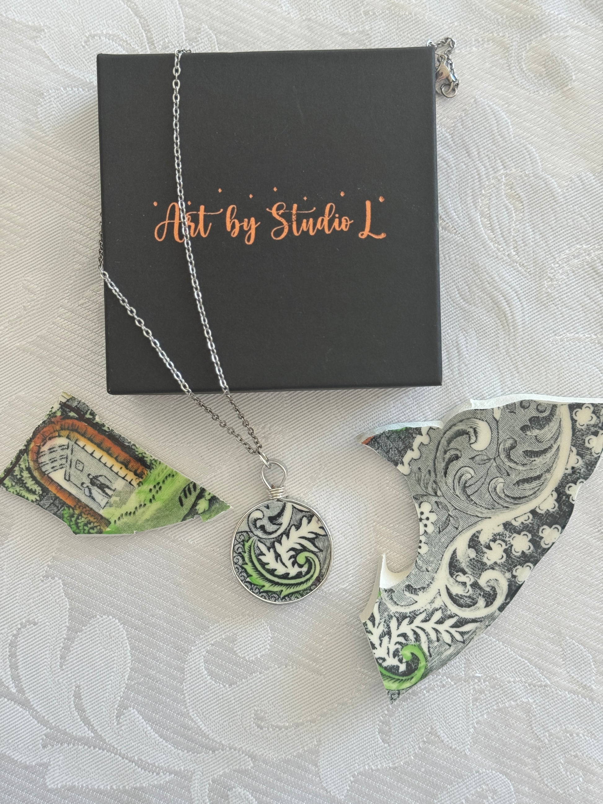 Necklace with a decorative pendant on a white textured surface with 'Art by Studio L' box.