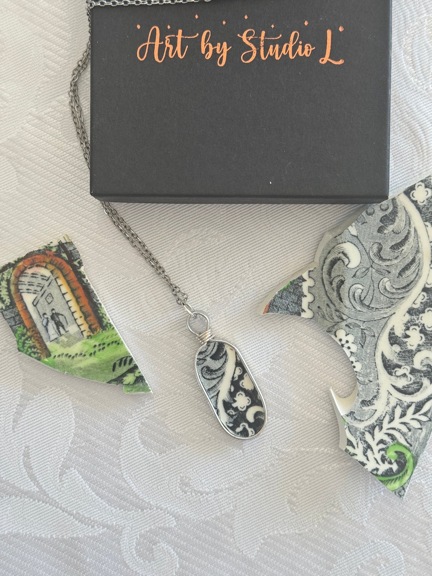 Necklace with a decorative pendant on a textured surface with 'Art by Studio L' packaging.