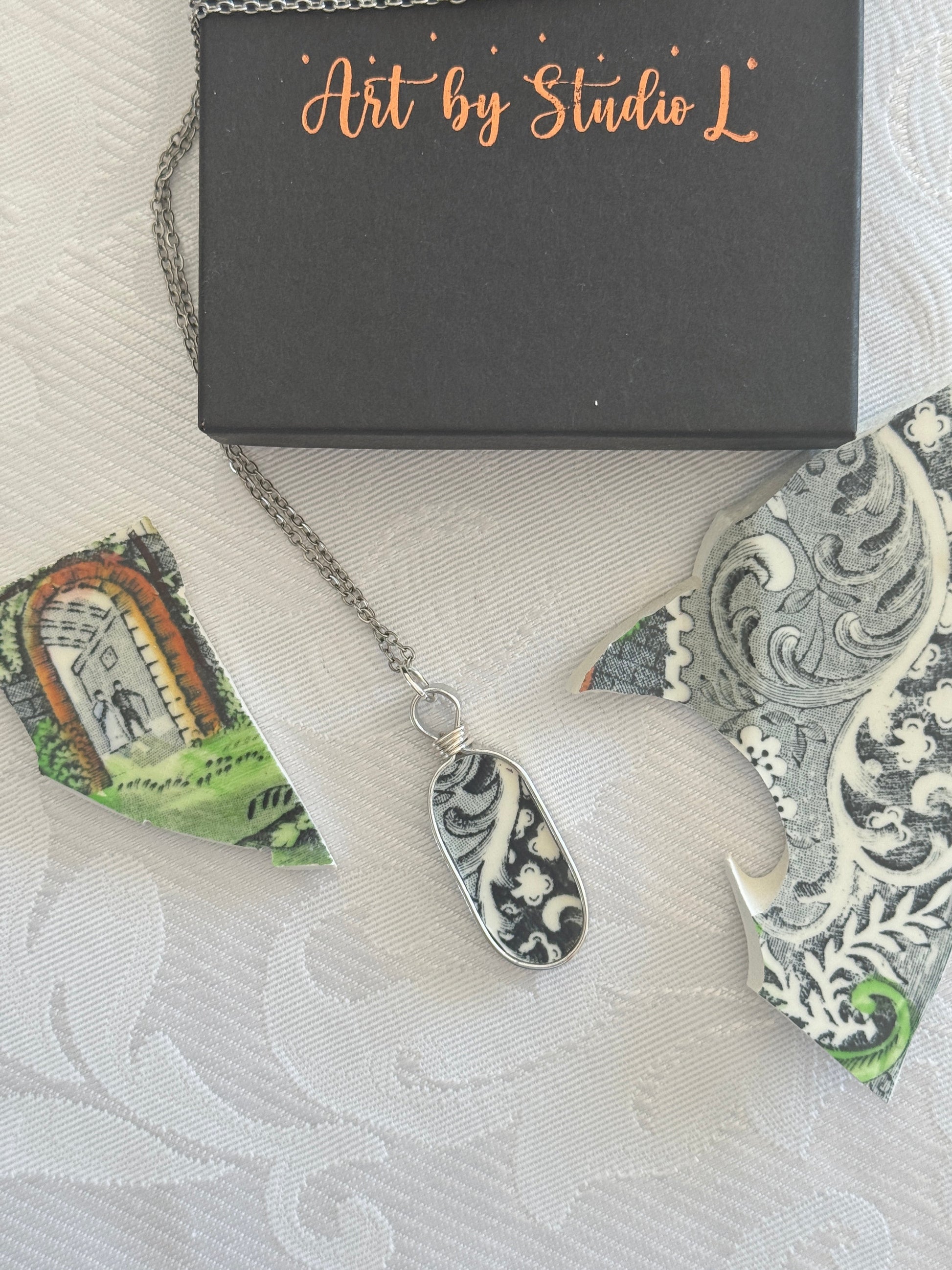 Necklace with a decorative pendant on a textured surface with 'Art by Studio L' packaging.