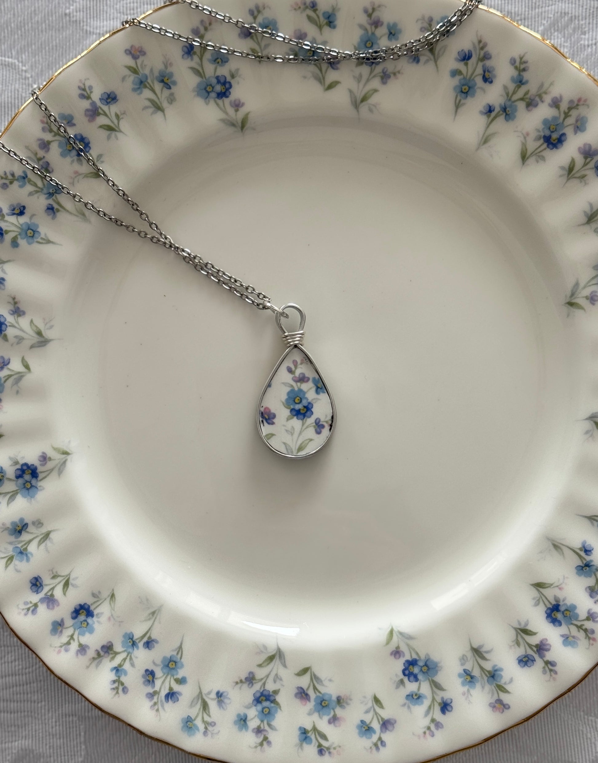 Teardrop-shaped pendant on a chain on a decorative plate with floral pattern