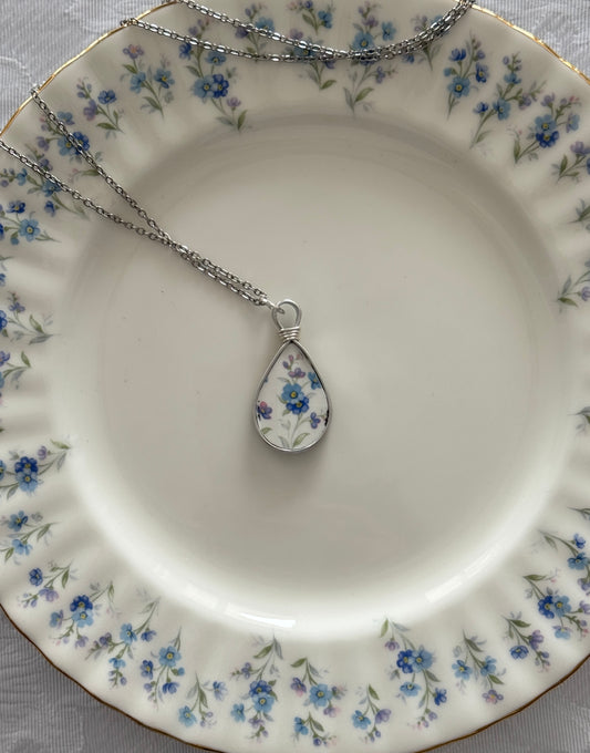 Teardrop-shaped pendant on a chain on a decorative plate with floral pattern
