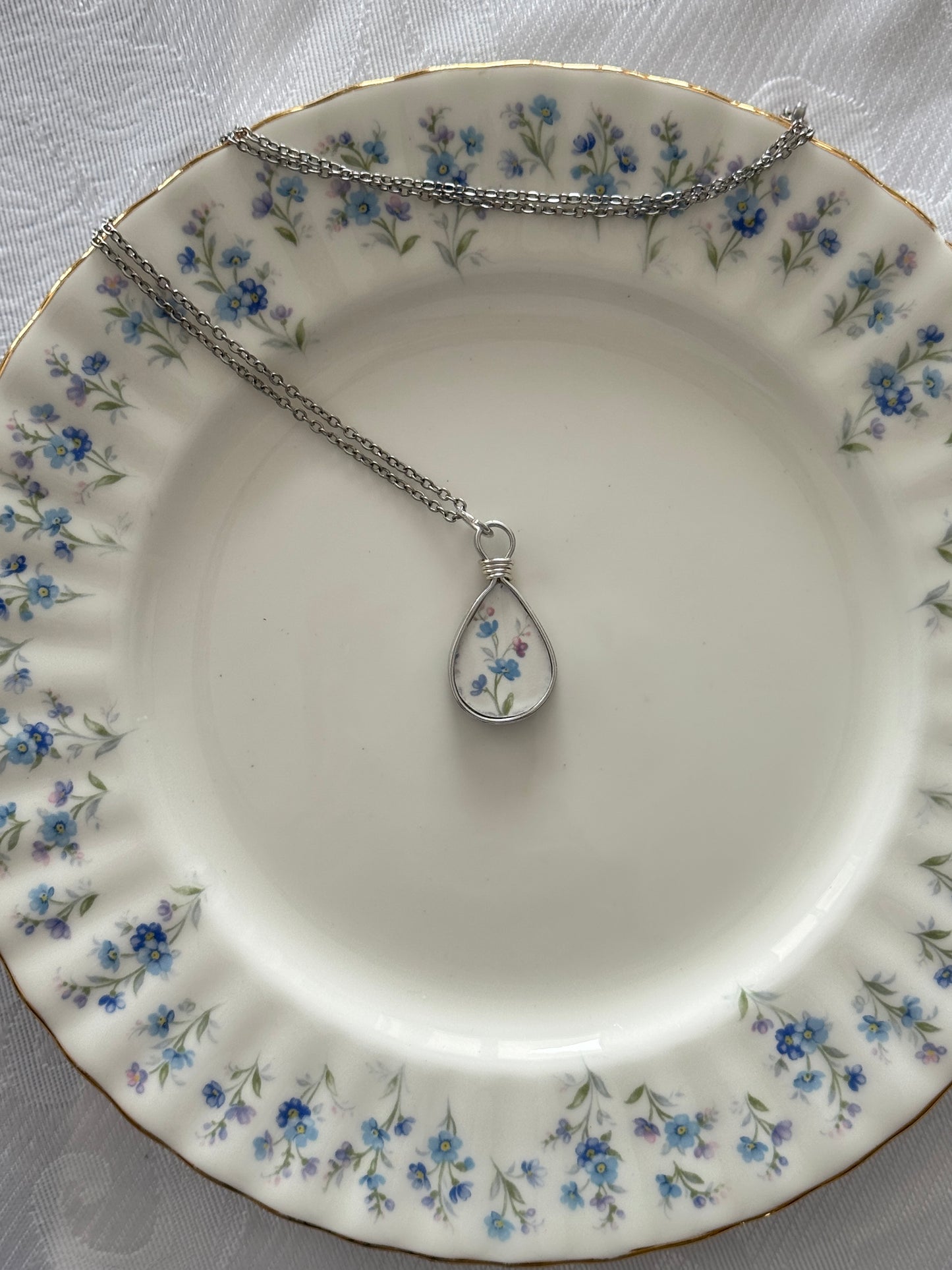 Necklace with a teardrop pendant on a decorative plate with floral pattern
