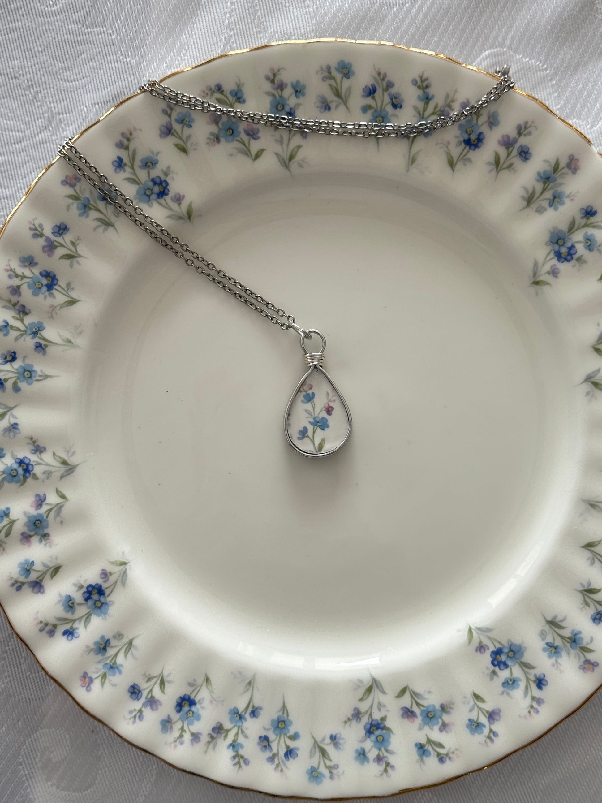 Necklace with a teardrop pendant on a decorative plate with floral pattern