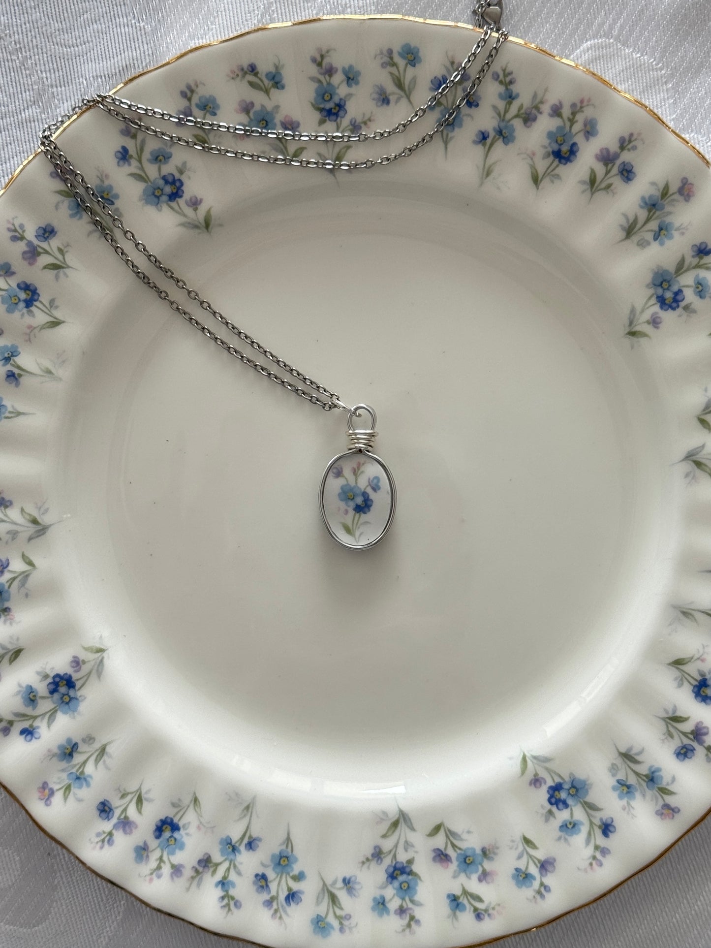 Silver necklace with a floral pendant on a decorative plate with floral patterns