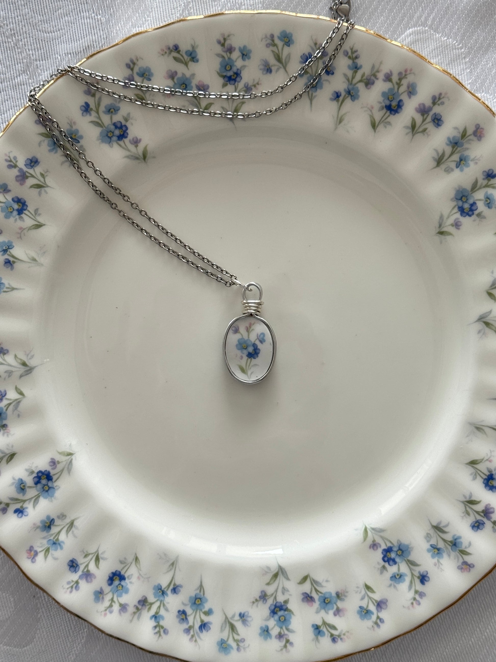 Silver necklace with a floral pendant on a decorative plate with floral patterns