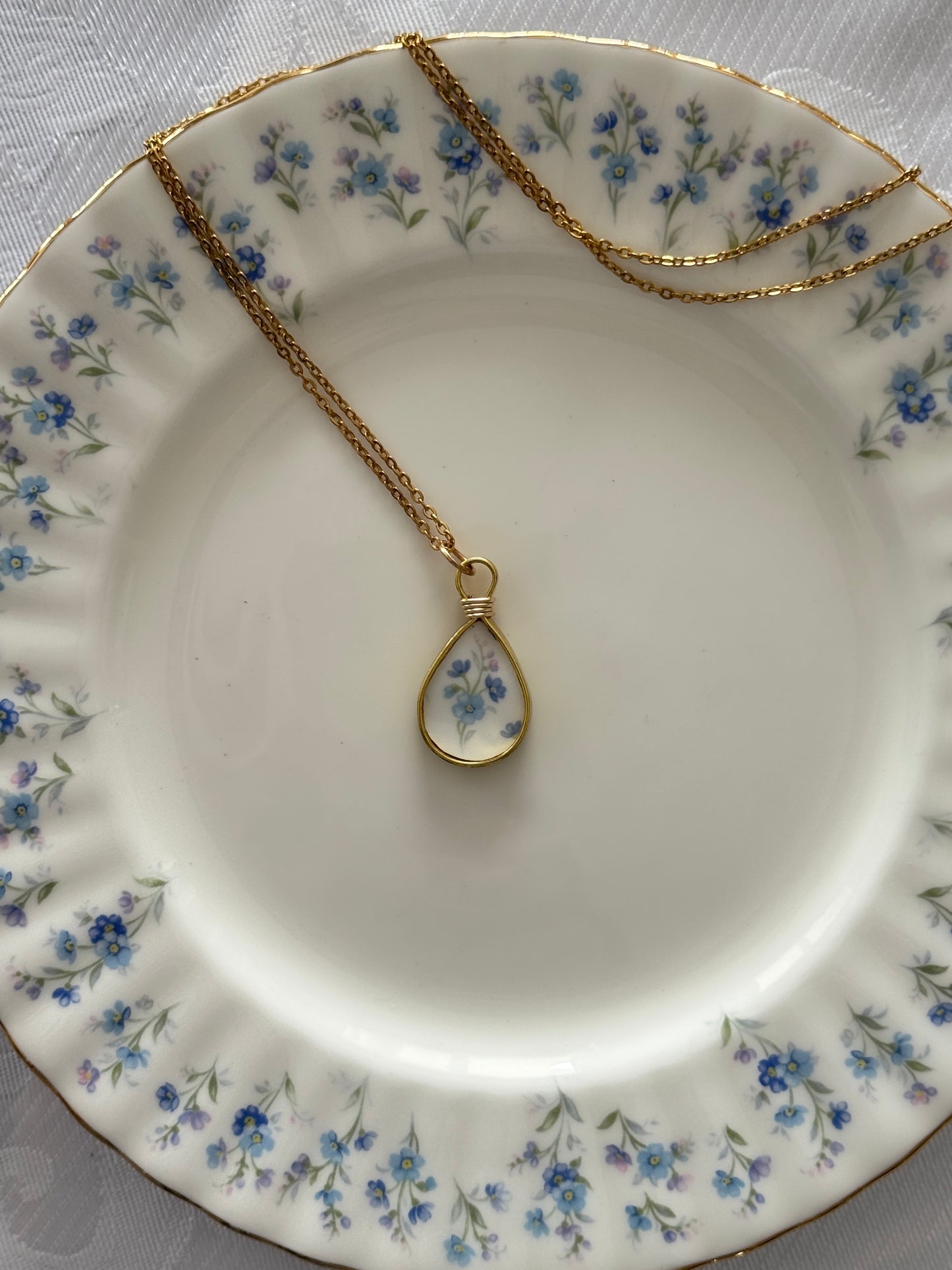 Gold necklace with a teardrop-shaped pendant on a floral-patterned plate