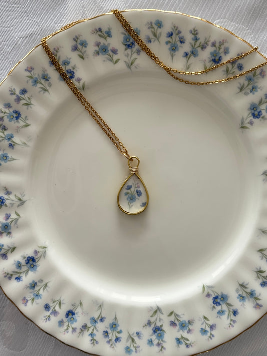 Gold necklace with a teardrop-shaped pendant on a floral-patterned plate