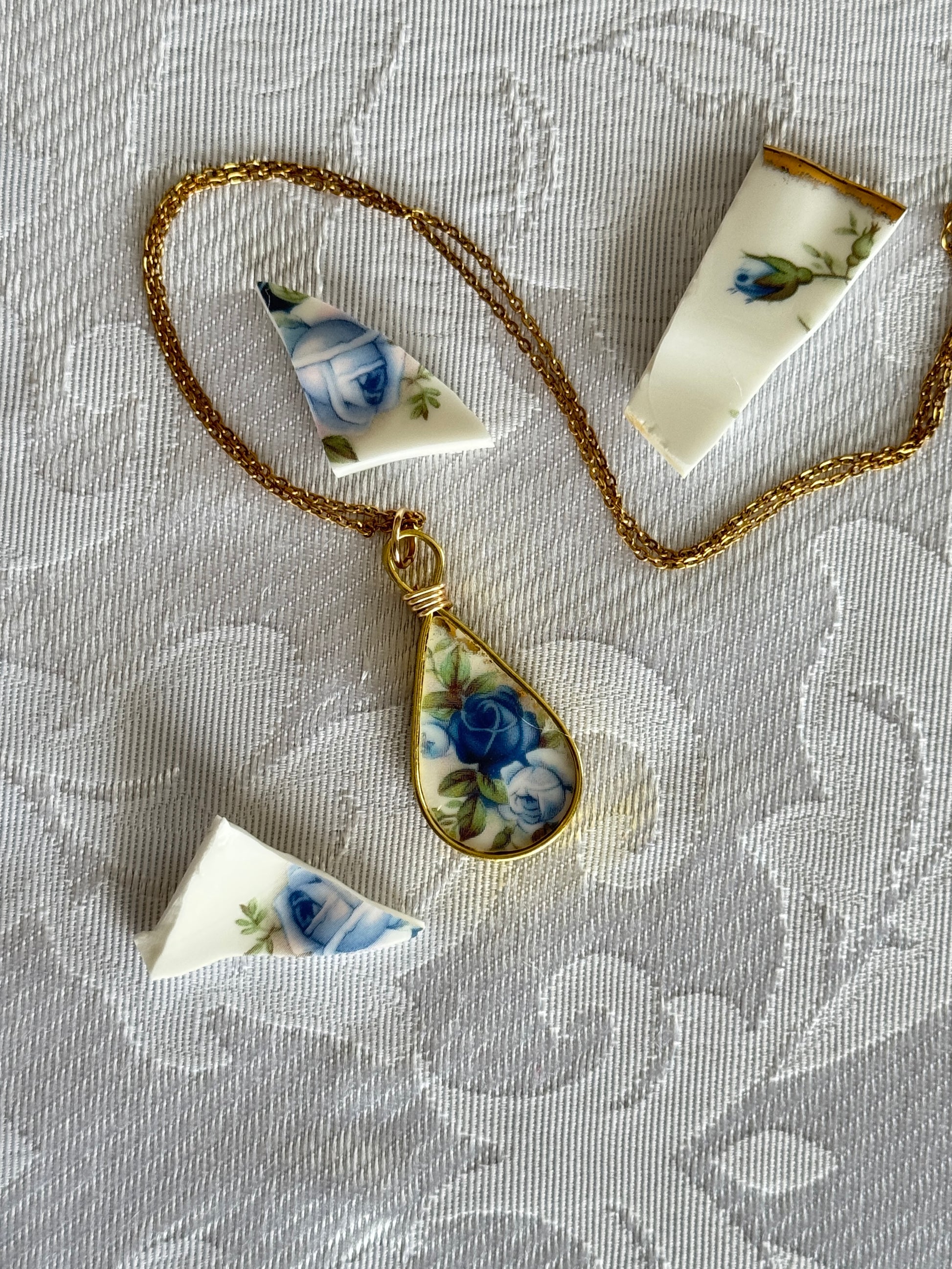 Necklace with a teardrop-shaped pendant featuring floral design on a textured fabric background