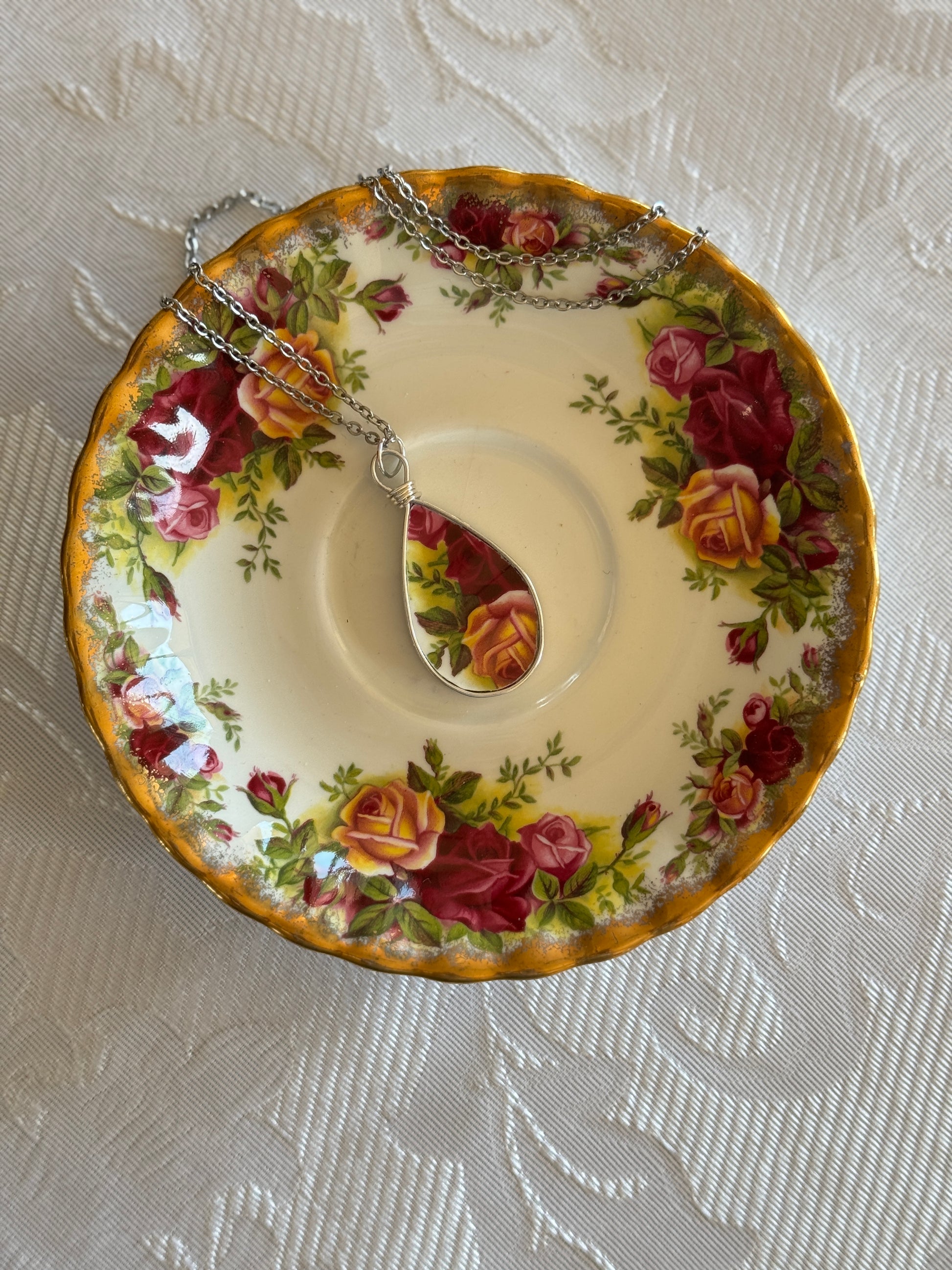 Decorative plate with floral design and a matching teacup-shaped pendant on a textured surface.