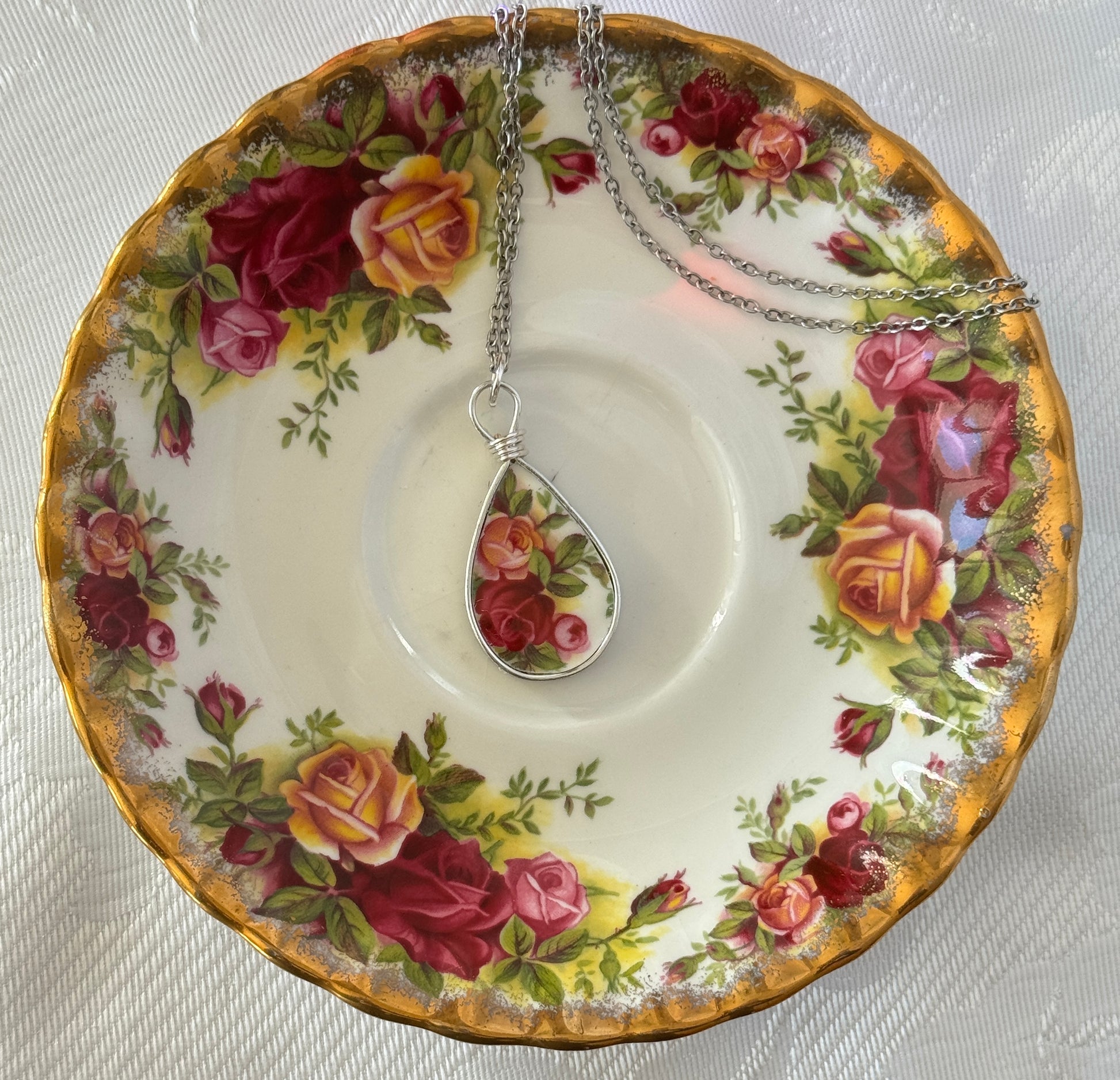 Tea cup saucer with floral design holding a teardrop-shaped pendant with floral pattern