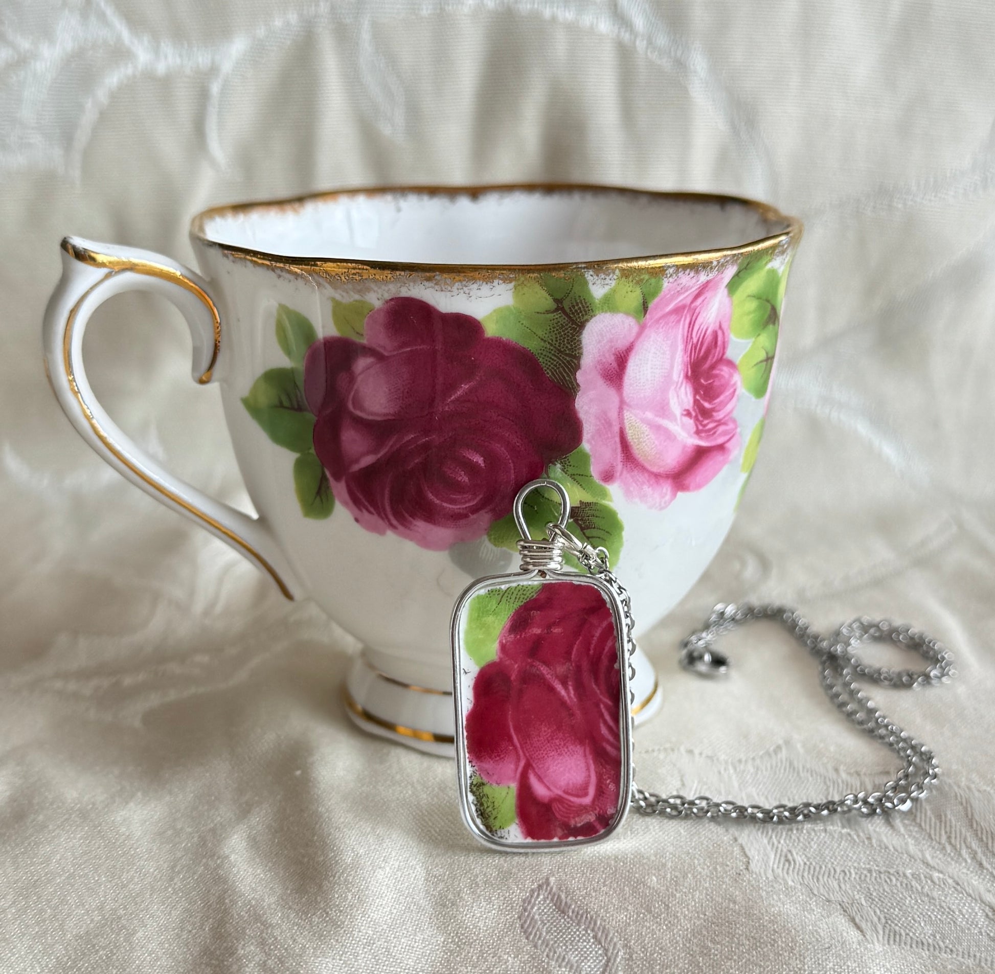 Teacup with floral design and matching pendant on a textured white surface