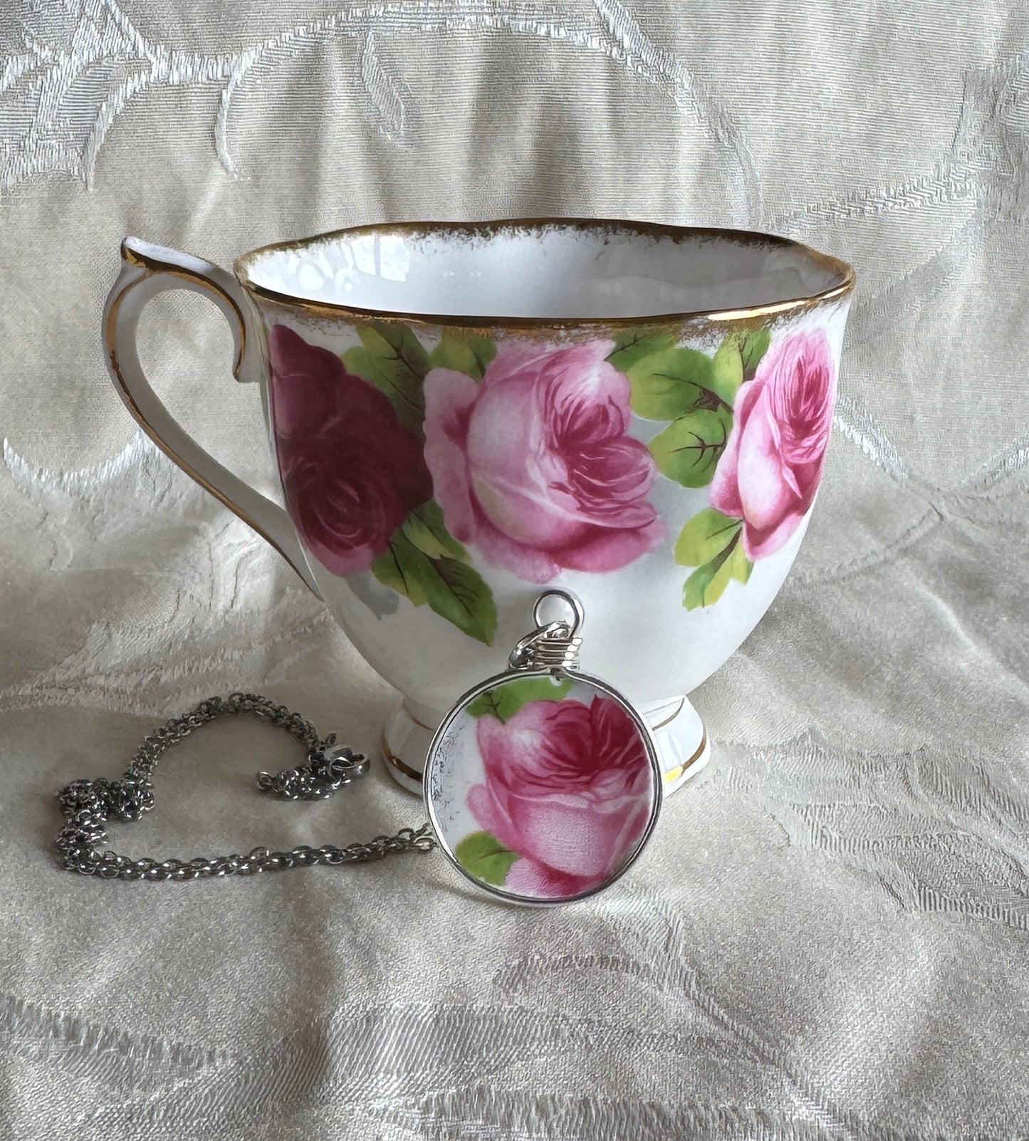 Teacup with floral design and matching pendant on a textured fabric background