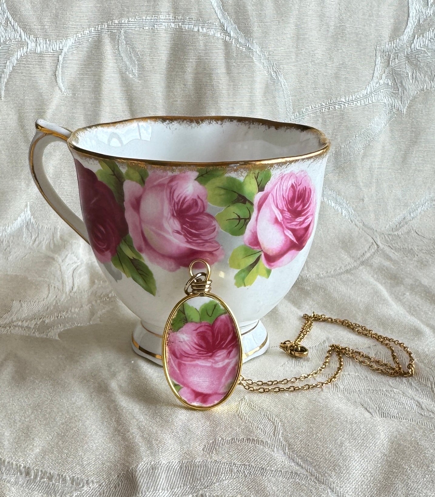 Teacup with floral design and matching necklace on a textured fabric background