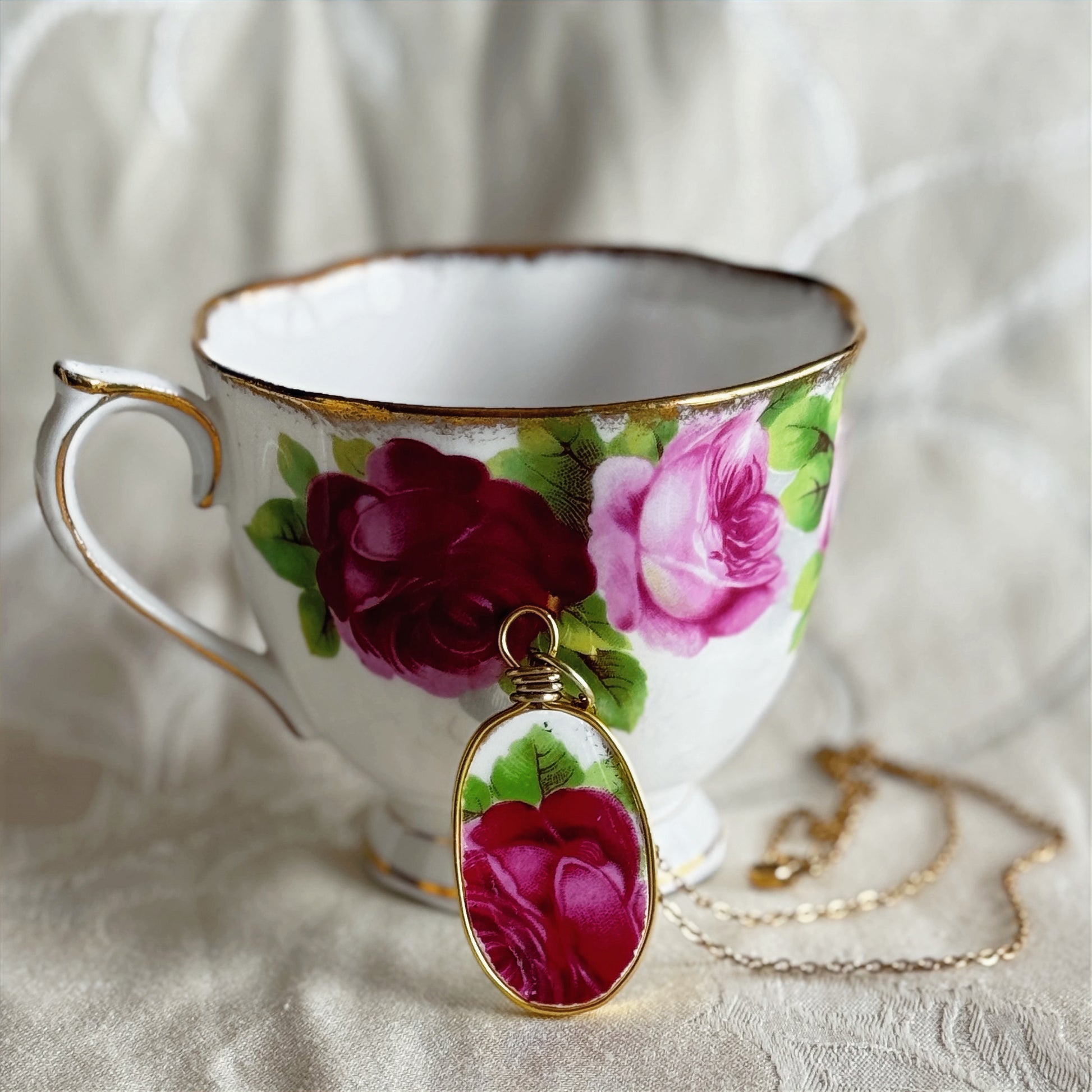 Teacup with floral design and matching pendant on a white fabric background