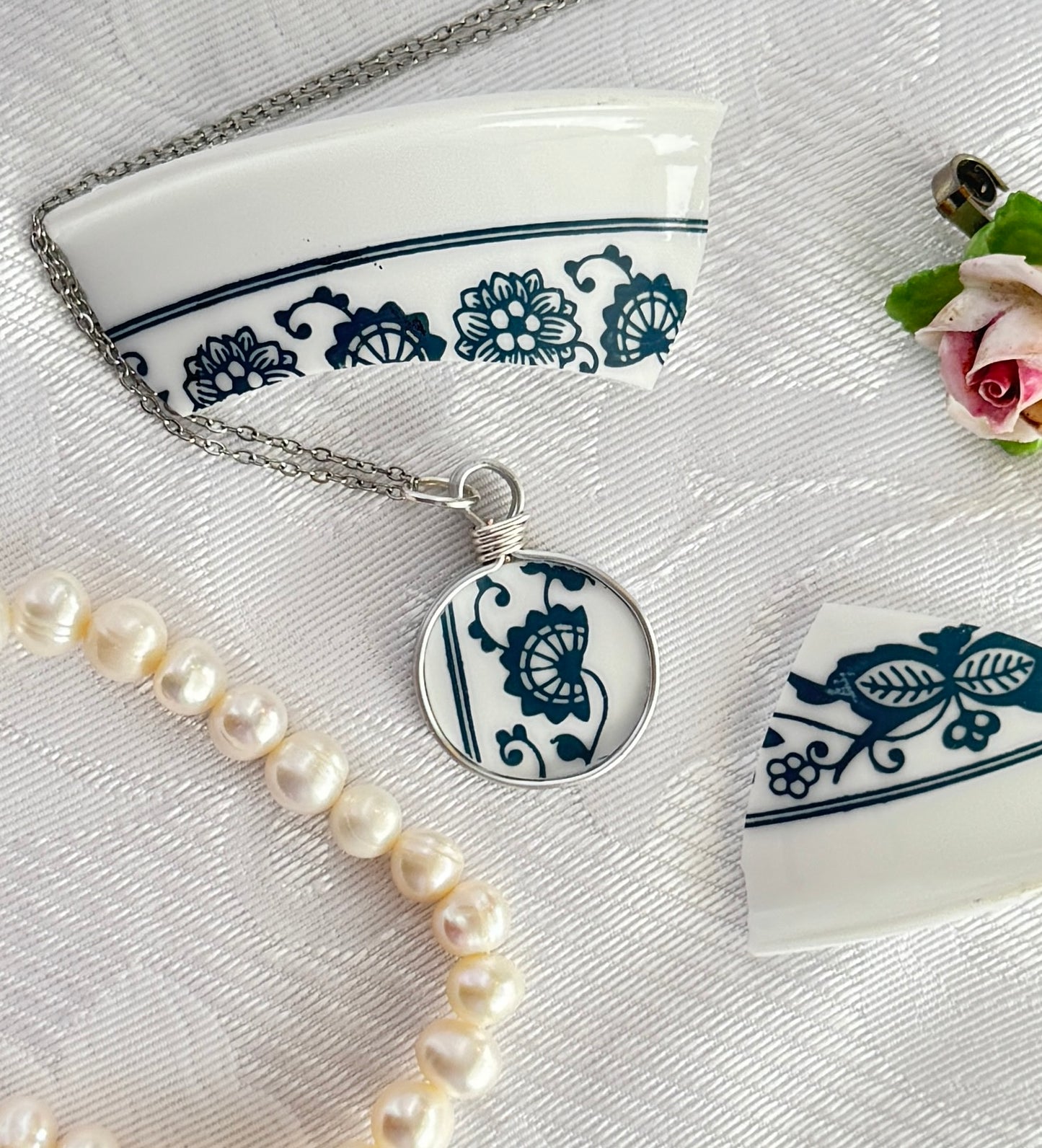 Necklace with a blue and white floral pendant on a white surface with decorative elements.