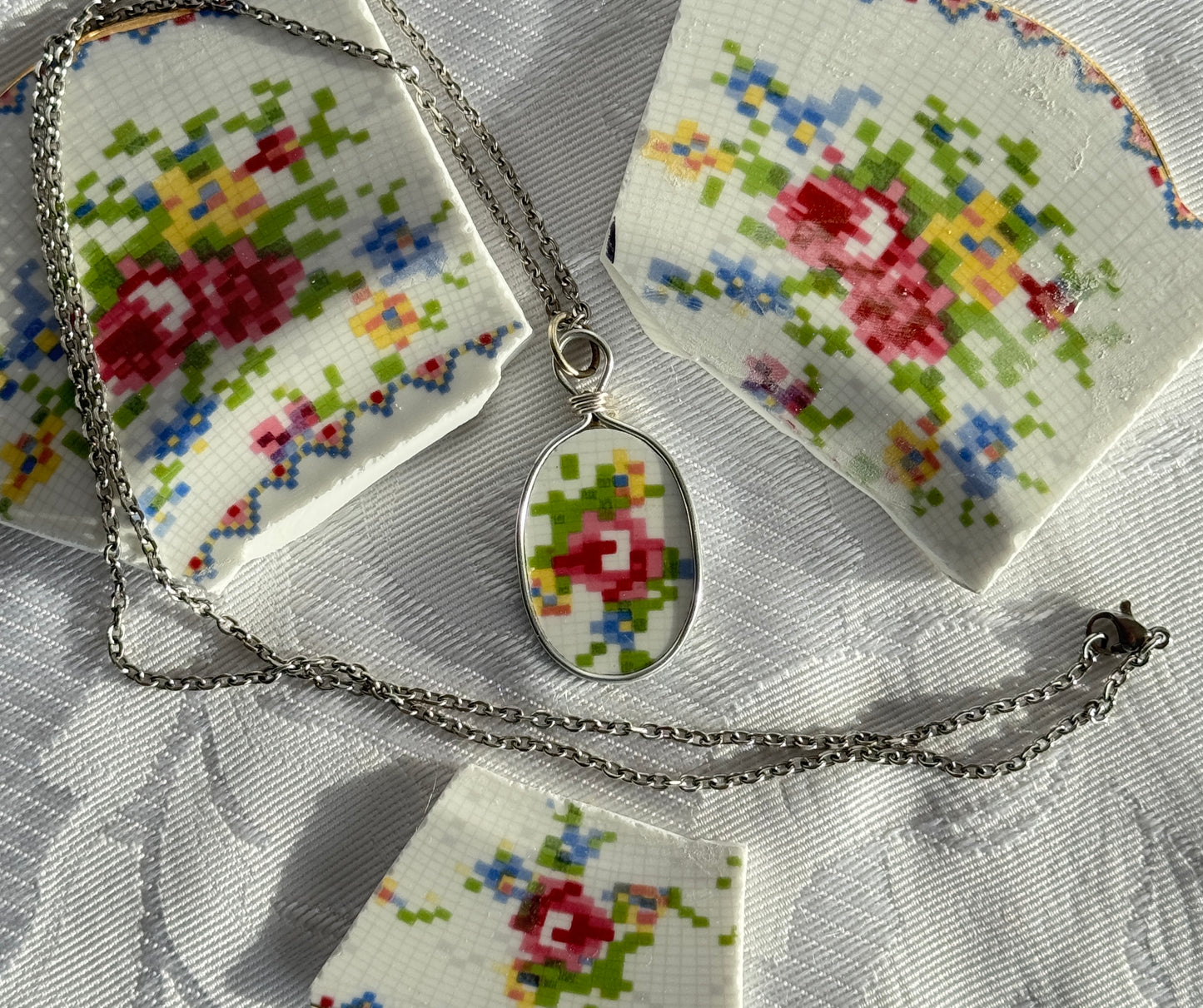 Necklace with a floral pendant on a cross-stitched fabric background