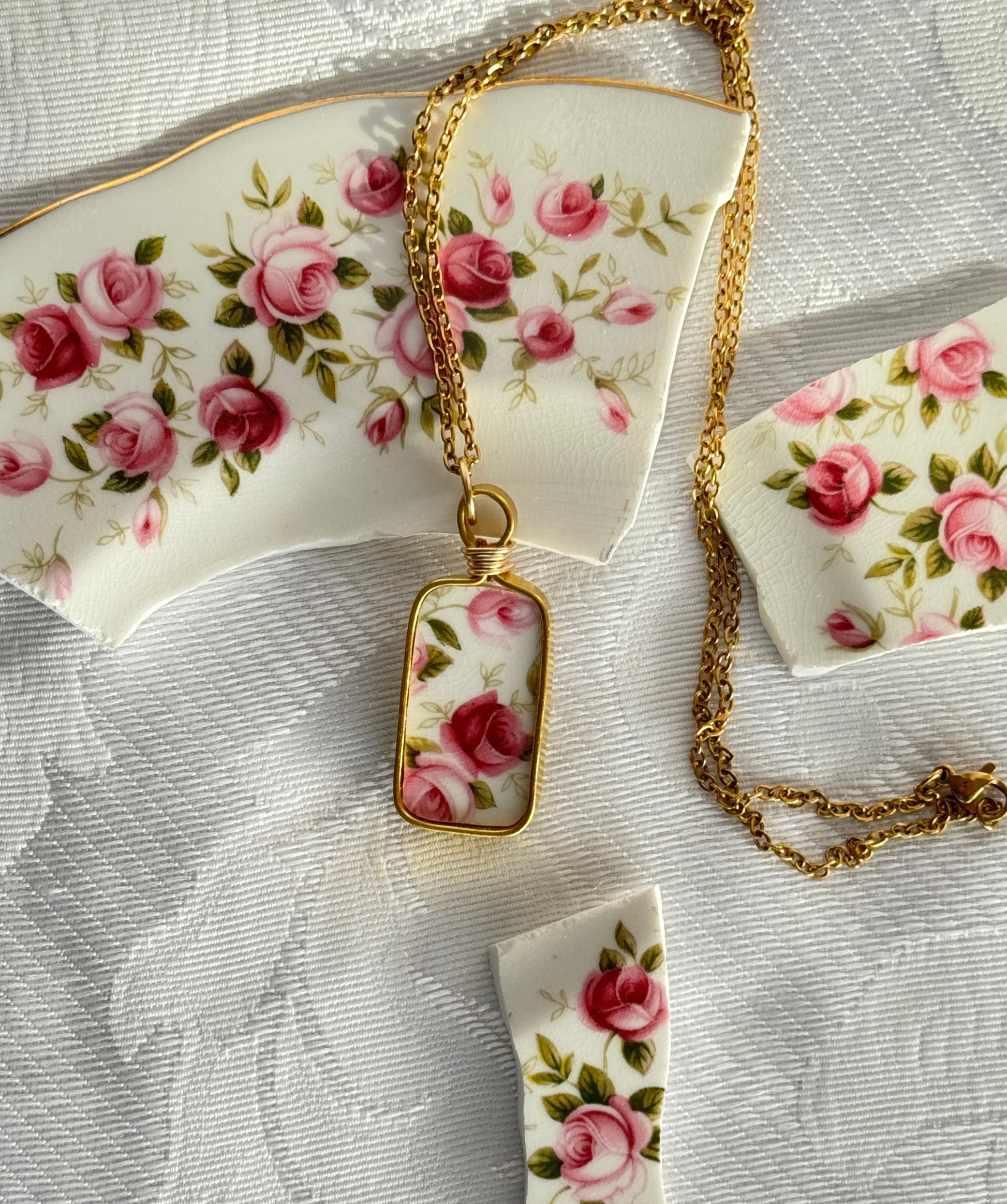 Gold necklace with floral pendant on a decorative plate with pink roses.