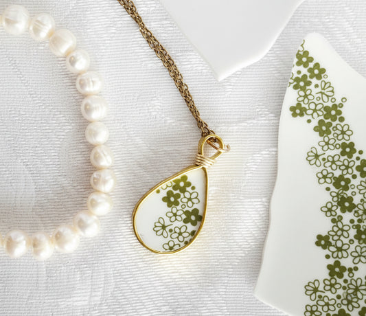 Pearl necklace with a teardrop-shaped pendant featuring floral design on a white background.
