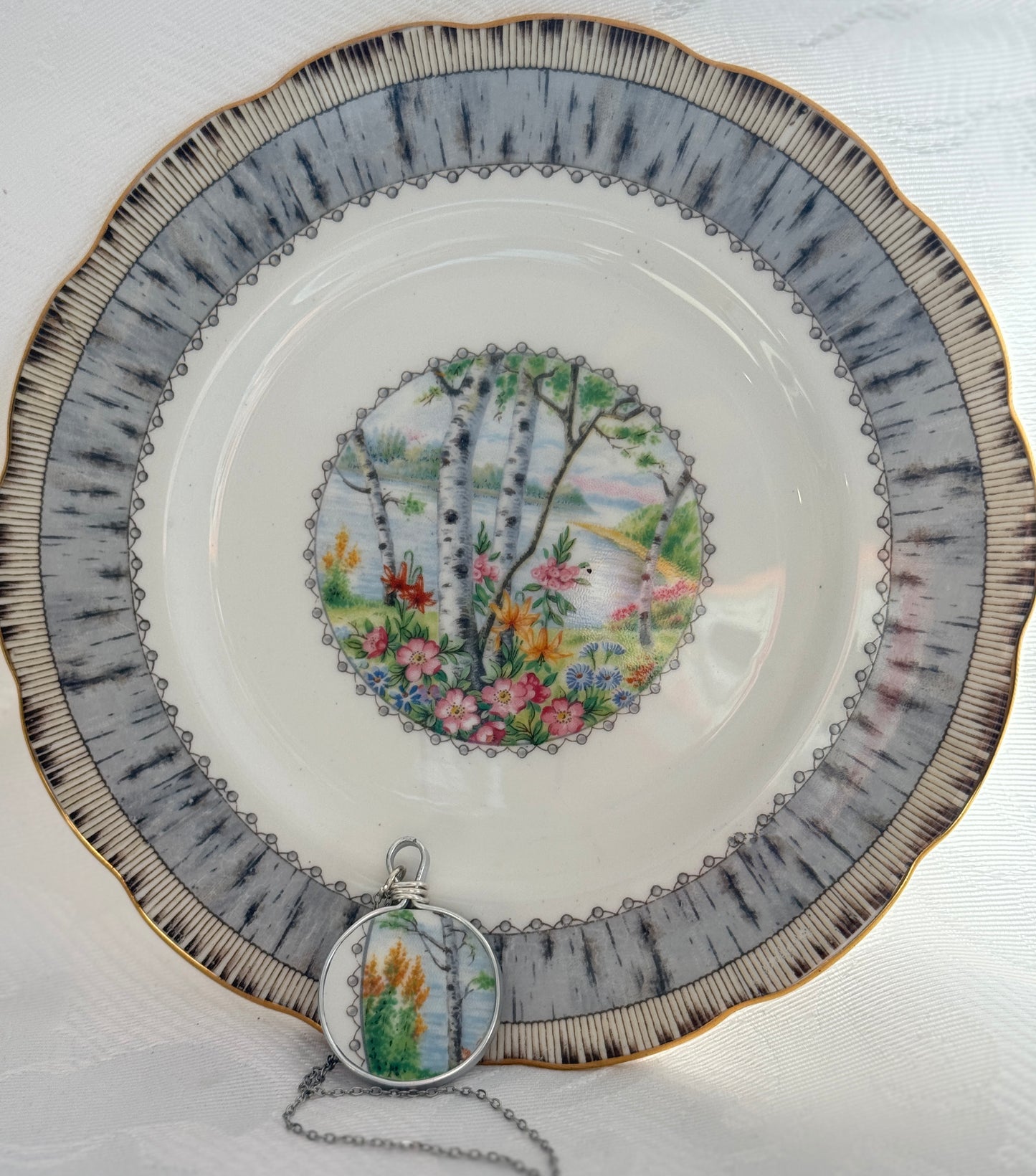 Decorative plate with nature-themed design and matching pendant on a white background