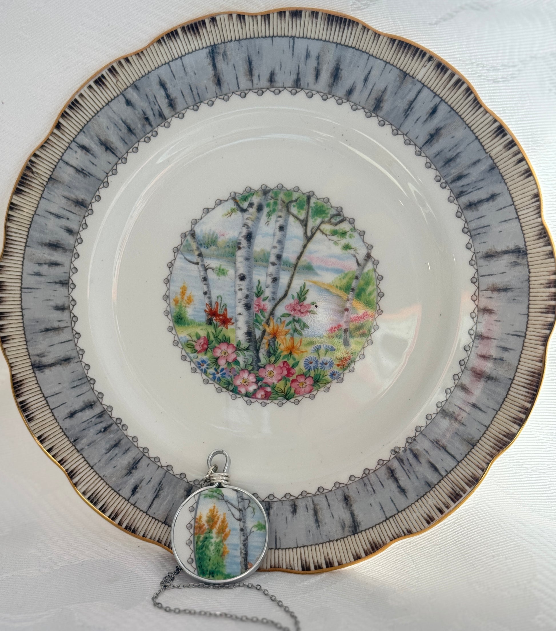 Decorative plate with nature-themed design and matching pendant on a white background
