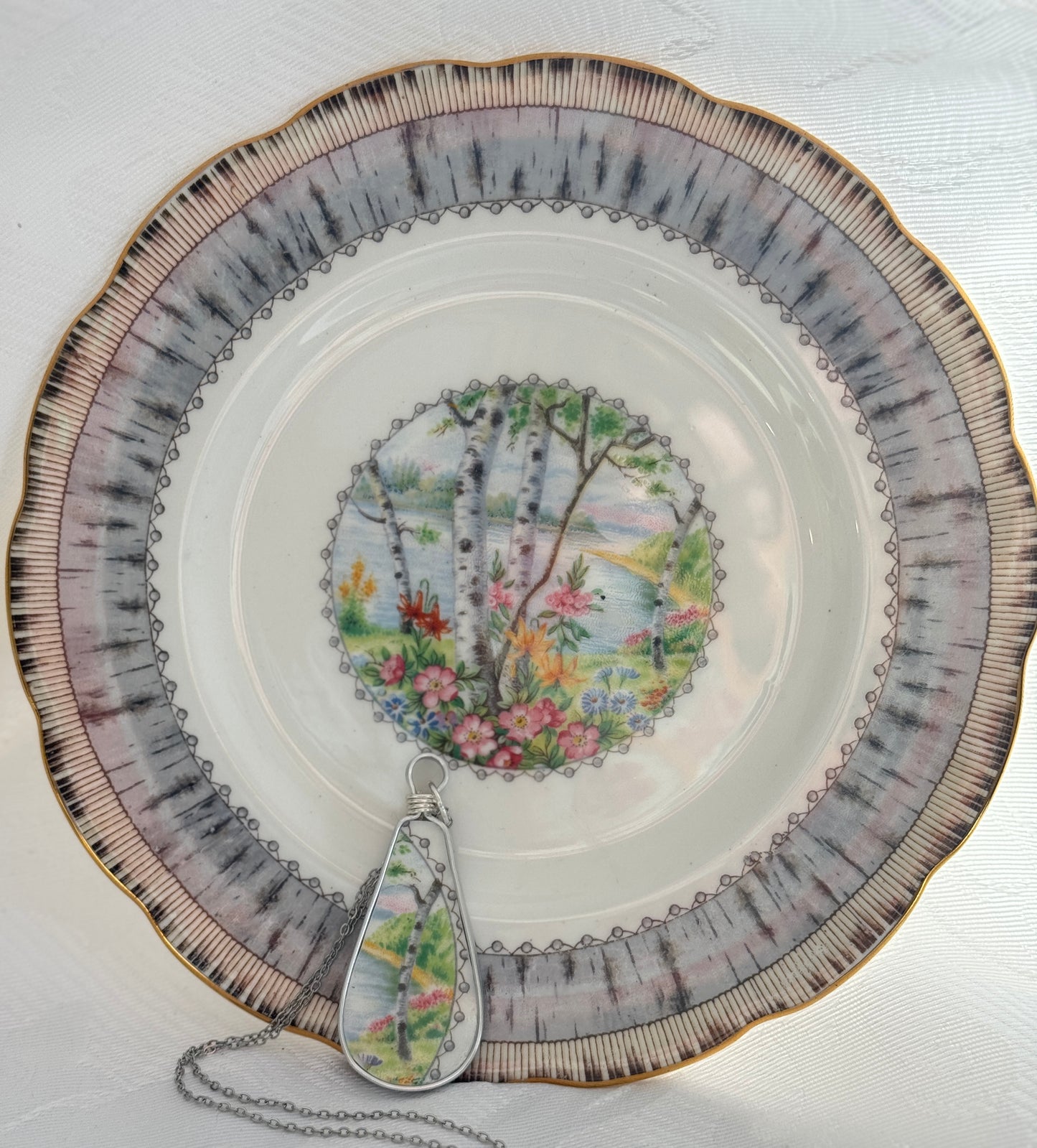 Decorative plate with floral design and a matching teardrop-shaped pendant on a white background