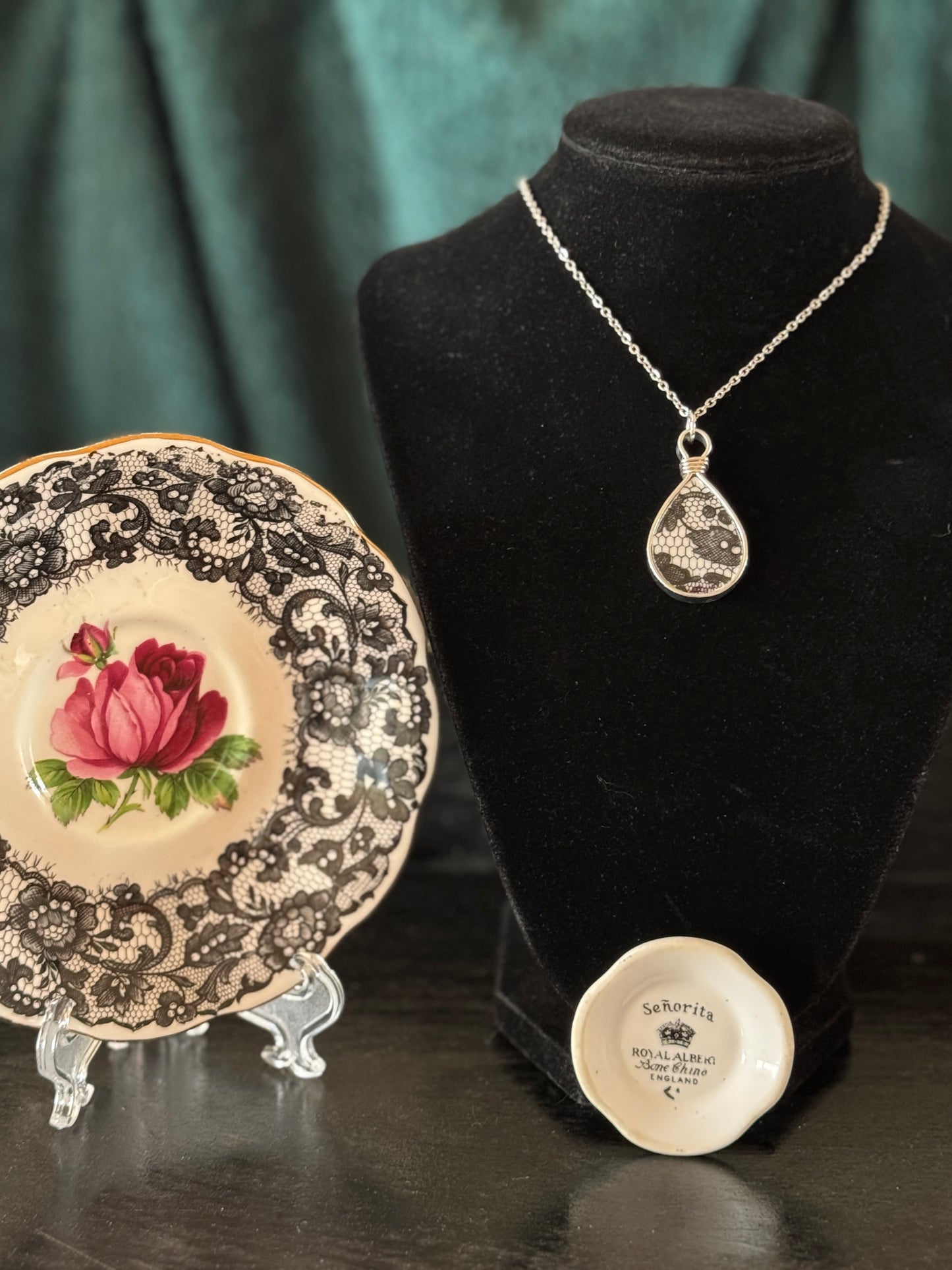 Necklace on a black velvet stand with a decorative plate featuring a rose design.