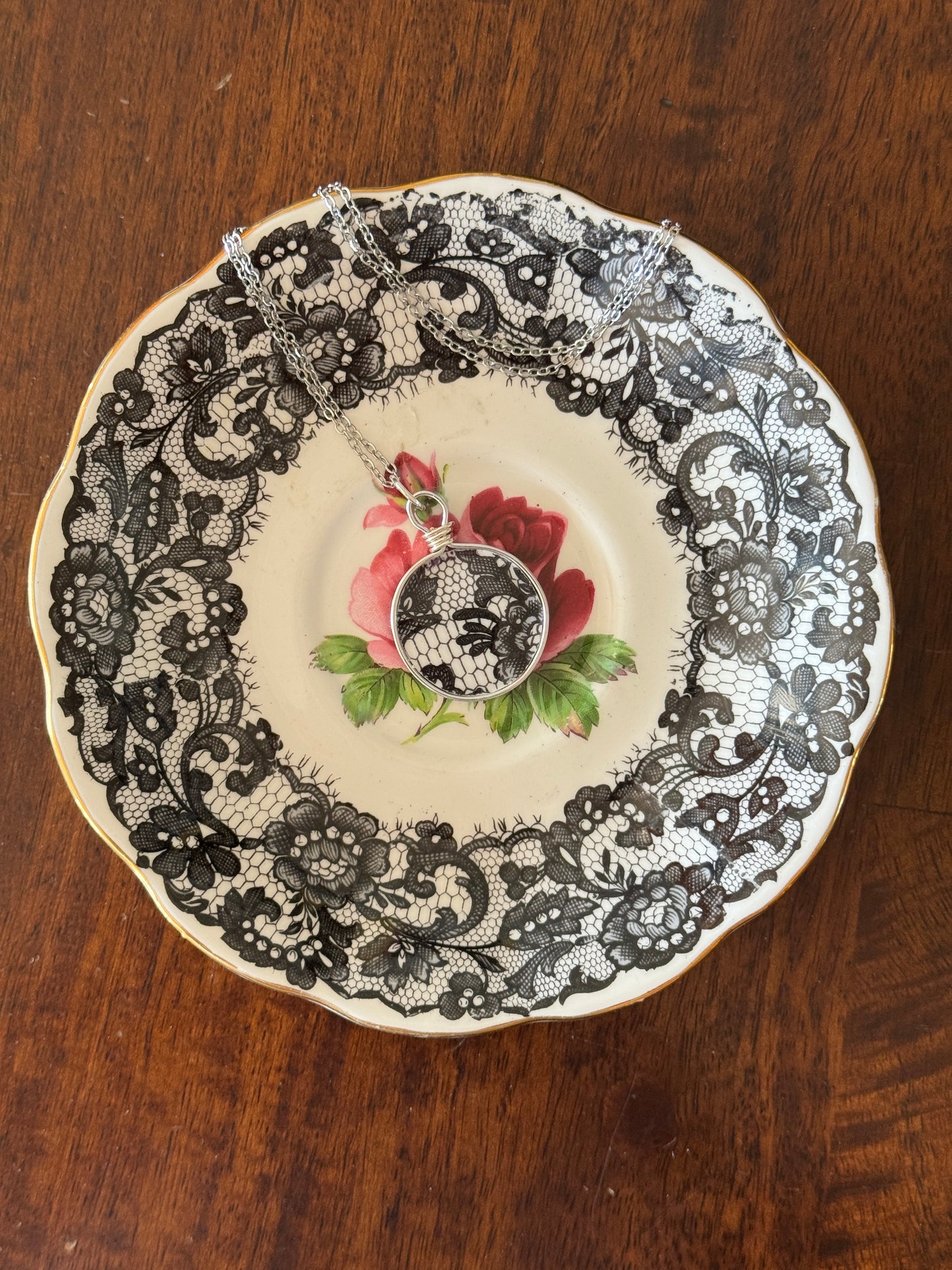 Decorative plate with black lace pattern and floral design on a wooden surface