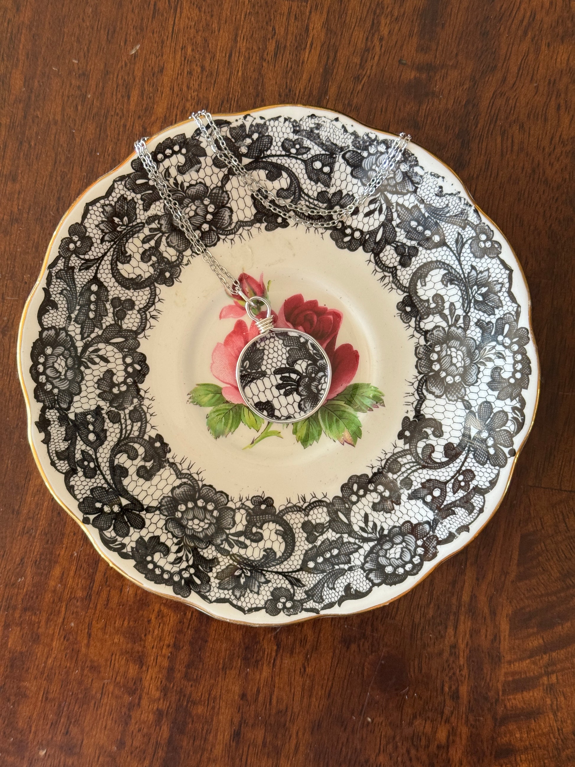 Decorative plate with black lace pattern and floral design on a wooden surface