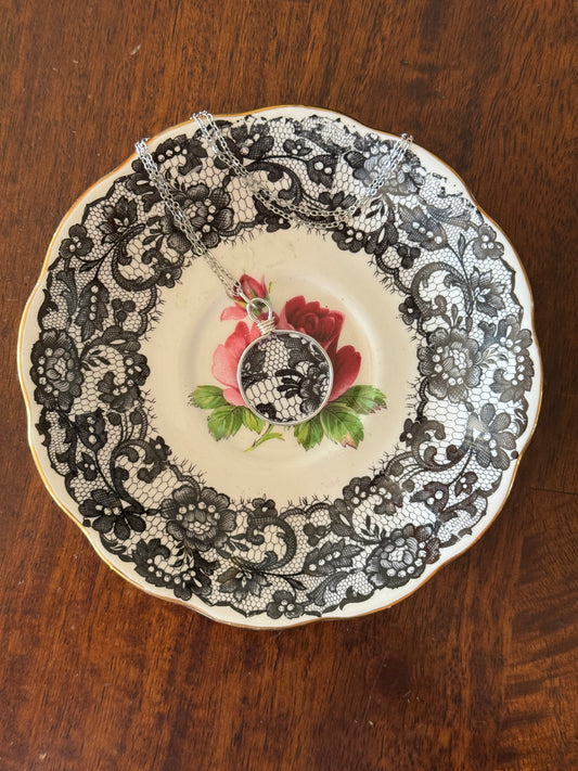 Decorative plate with black lace pattern and floral design on a wooden surface