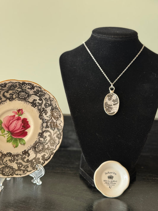 Necklace on a black velvet stand with a decorative plate and small round object in the foreground.